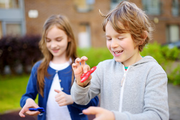 Two funny friends playing with fidget spinners on the playground. Popular stress-relieving toy for school kids and adults.