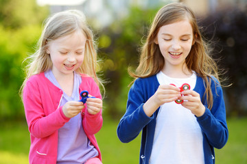 Two funny sisters playing with fidget spinners on the playground. Popular stress-relieving toy for...