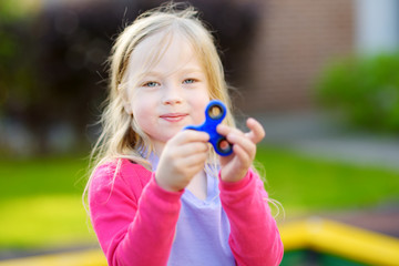 Fototapeta premium Cute school girl playing with fidget spinner on the playground. Popular stress-relieving toy for school kids and adults.