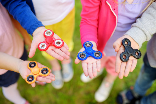Four school children playing with fidget spinners on the playground. Popular stress-relieving toy for school kids and adults.