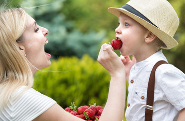 Mom makes son eat small ripe fragrant strawberries.