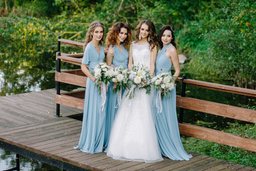 Obraz na płótnie Canvas Stylish bridesmaids with a bride stand near the water