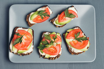 Healthy green veggie food concept. Yammy toast with cream cheese, avocado and juicy red tomato on grey plate and table.