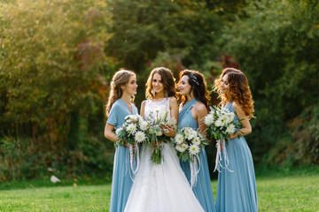 Beautiful slim bride walks with friends in a blue dress at sunset