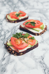 Healthy green veggie food concept. Yammy toast with cream cheese, avocado and juicy red tomato on grey and white marble table.