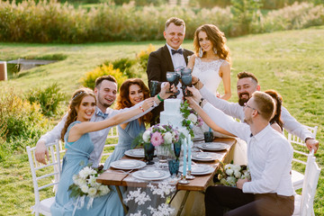 Positive guests celebrate at the table the wedding of their friends in the nature