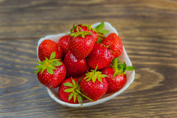 A small white porcelain bowl filled with juicy fresh ripe red strawberries. Textured table top. Fresh strawberries. Strawberries in a Bowl