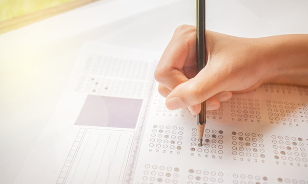hand student testing in exercise and taking fill in exam carbon paper computer sheet with pencil at school test room, education concept