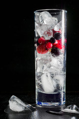 Glass of ice with berry gooseberries red black currants and water. Refreshing cocktail. Summer drink.