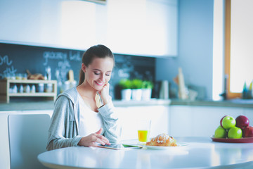 Young woman with orange juice and tablet in kitchen.