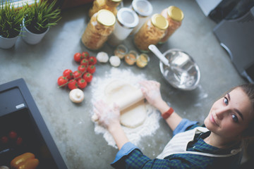 Beautiful woman cooking cake in kitchen standing near desk.