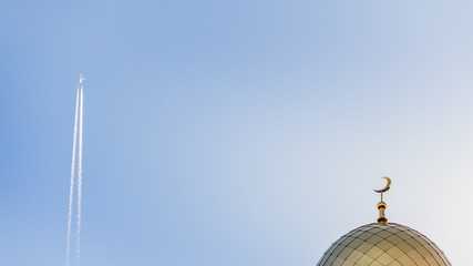 On the right is the golden minaret of the Islamic mosque, on the left the plane flying far into the blue sky.