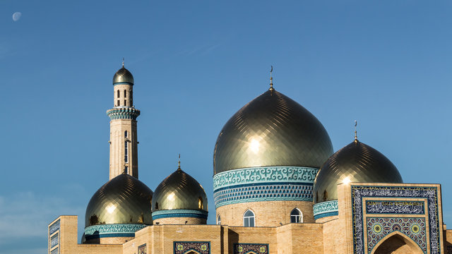Beautiful mosque of yellow bricks, golden shine of minarets, against the background of the moon in blue sky. Summer, 2017 Kazakhstan, Kostanay.