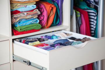 Neatly folded clothes with accessories in chest of drawers