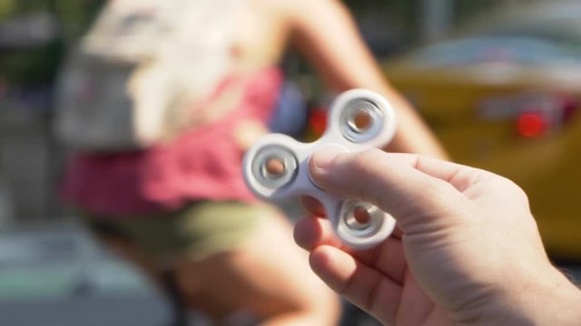 An unidentified male plays with a hand spinner toy in the downtown area of a large city. Slow Motion, shot at 180fps.  	