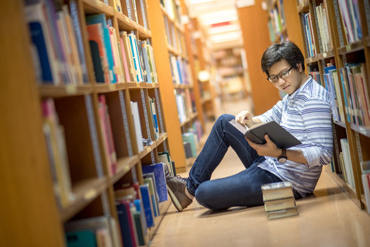 Young Asian man university student reading book in library, education research and self learning in university life concepts