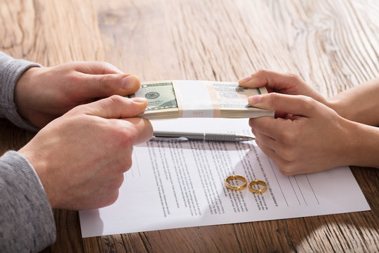 Couple's Hand Holding Currency Over The Divorce Agreement