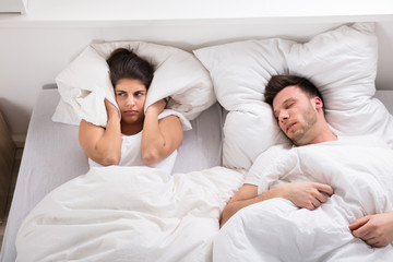 An Angry Woman With Snoring Husband On Bed
