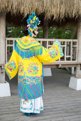 Fototapeta premium beautiful chinese girl in traditional chinese dress with long sleeves and hat with pompons standing back outdoor and turning hand into prifile