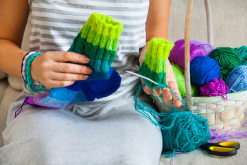 A woman in a gray dress knit socks from colored yarn. Balls of colored yarn are in the basket.