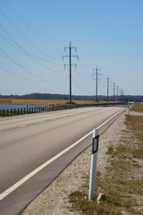 Fototapeta premium Straight road and high-voltage power transmission line against blue sky