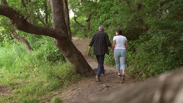 Cheerful middle-aged couple walking in forest Park, man funny jumps to the side.