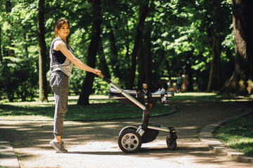 Fototapeta na wymiar Series photo of happy sporty mother with baby pram workout and warming up bebore jogging in summer park. Full height
