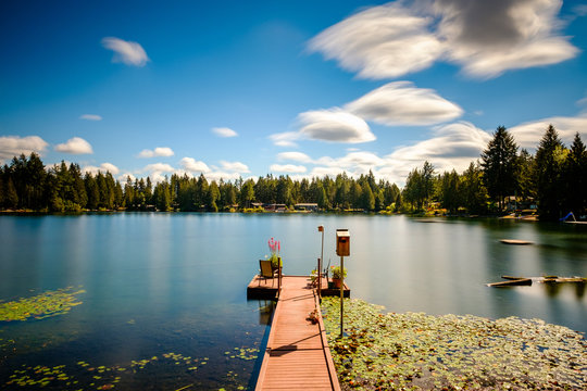 Long exposure of a lake with a dock and streaky clouds - Powered by Adobe