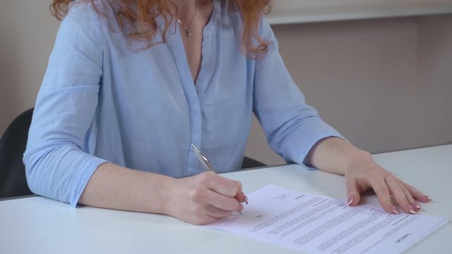 Closeup detail woman hands sing contract and handwriting date. Woman sitting at the white desk with documents.