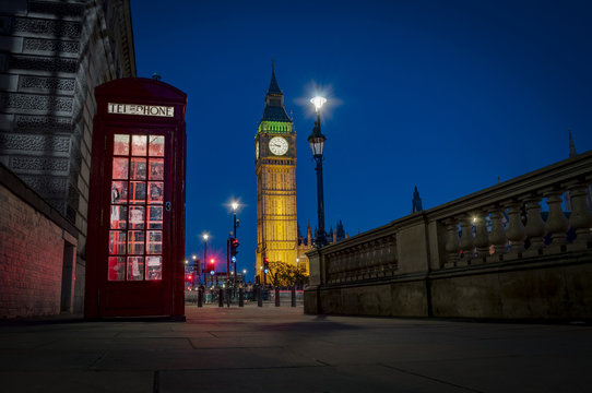 Fototapeta Traditional red phone booth or telephone box with the Big Ben in the background, possible the most famous English landmark, at night in London, England, UK