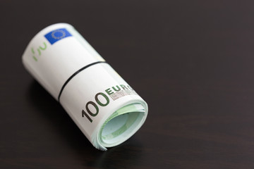 Roll of one hundred euro banknotes on wooden black table