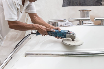 Yacht maintenance. A man polishing side of the white boat in the marina