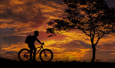Obraz premium Silhouette, Adventurer Backpack stops the bike under the tree,Background Sunset.