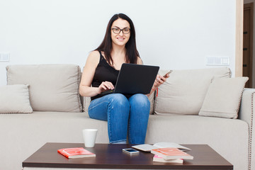 Smiling young woman sitting on couch and using laptop and drink tea