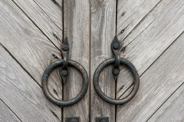 Vintage dark wooden gates with round metal handles in the form of rings. Background.