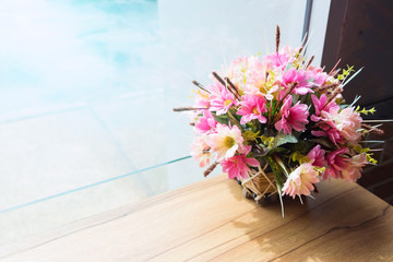Pink flower made from fabric in wood basket on wooden table near the glass wall in rainy day. soft tone.