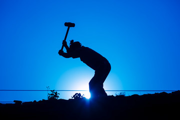 Action silhouette labor man hitting his hammer over sunset. Image made blue tone.