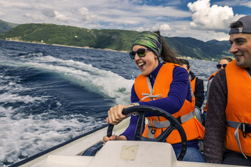 Portrait of young and attractive people, friends sitting in the motorboat close up. Girl is having fun driving the boat. You can see waves on background. Norway.