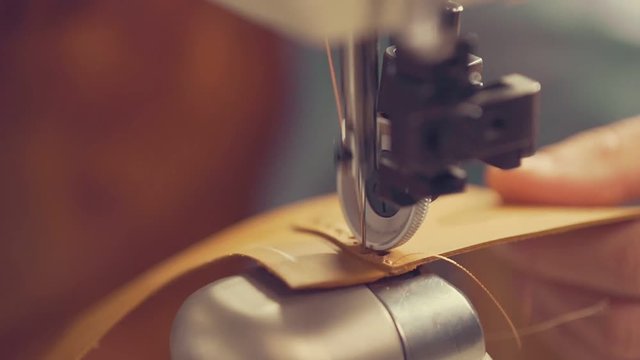 The master makes shoes in the workshop. Side view of using sewing machine to make seam