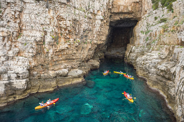 View from the rock cliffs of kayakers exploring the crystal clear Mediterranean waters of a cove...