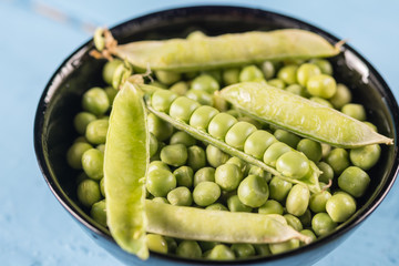 Fresh raw green peas in the bowl on the wooden planks table with copy space