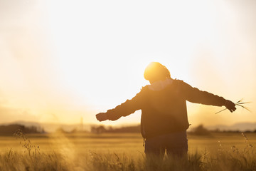 Middle aged caucasian woman standing in the sunlit field with open arms, embracing nature