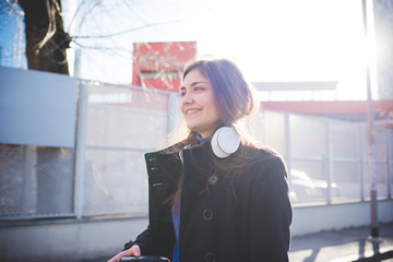 Portrait young woman outdoor back light looking away smiling headphones around neck - emancipation, freedom, girl power concept