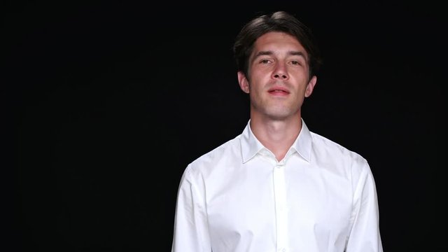 Confident calm brunette man looking camera while standing isolated over black background 