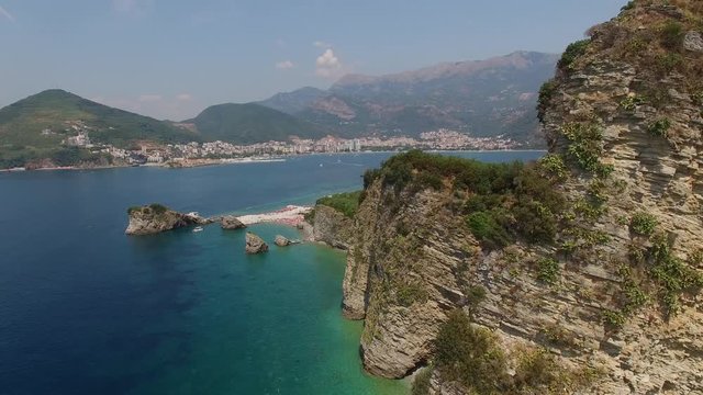 Island of St. Nicholas near Budva. Beautiful Montenegro nature rock mountains city. Beach tourist people rest swim. Cliff rocks above sea. Aerial helicopter flight close. Summer hot day