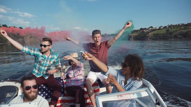 Group of diverse excited people sailing on boat playing with colored smoke bombs and celebrating Independence day.