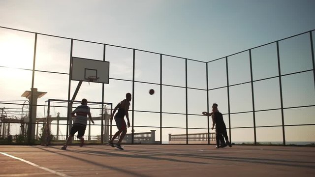 Sportive happy people playing streetball on sunlit playground in slowmotion. Footage with sun flare