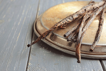 Dried vanilla sticks and metal plate on wooden background, closeup