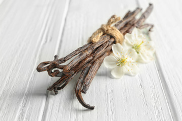 Dried vanilla sticks and flowers on light wooden background, closeup