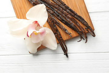 Dried vanilla sticks, flower and board on light wooden background, closeup